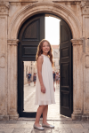 Rozalia girls' white pleated dress in front of a stone gateway – front view