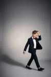 Sam boys' black occasion set with bow tie – boy in motion on a grey background, open blazer, full length